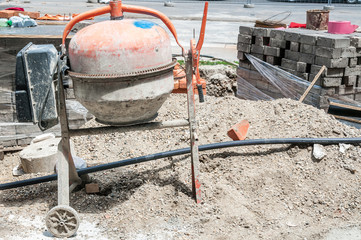 Small construction work site with dirty plaster mixer, pile of sand, stack of pavement tiles for pedestrians sidewalk in the city