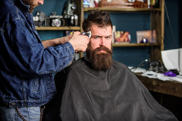 Barber with clipper trimming hair on temple of client. Hipster lifestyle concept. Barber with hair...