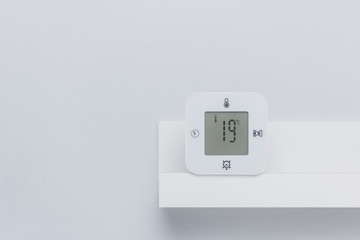 A white digital thermometer on the shelf with negative space. Room temperature concept.