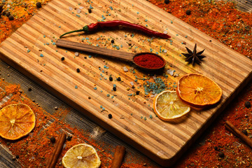 Culinary arts concept. Spices scattered around cutting board. Spoon with spices on wooden texture. Spoon filled with cinnamon, grinded red pepper and curcuma powder lay on cutting board