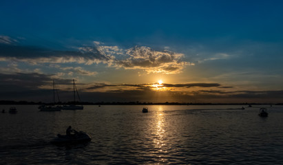 Fototapeta na wymiar Power boats, sailboats and jet skis on the Guaiba river having a pleasure time during a wonderful sunset with blue and orange colors between some clouds in the sky
