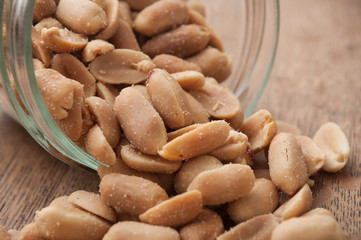 closeup of salted peanuts falling from glass container on wooden background