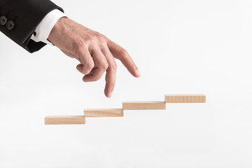 Businessman walking his fingers up steps formed by wooden blocks