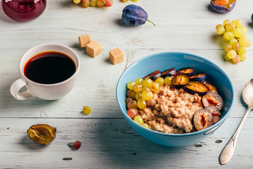 Porridge with fresh plum, green grapes and cup of coffee.