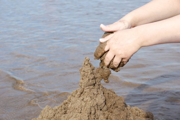 the hand of the child builds a sand castle on the beach on the background of water