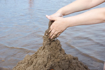 the hand of the child builds a sand castle on the beach on the background of water