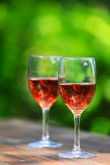 Two glasses of Shinning Rosé Wine on wooden table, defocused bright and fresh green outdoors background 1