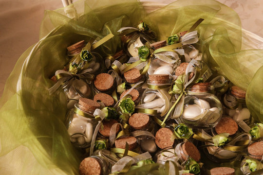 bellissime bomboniere con confetti fatte in vetro con tappo di sughero e fiocco verde, contenute in un cesto di vimini bianco