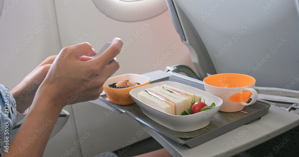 Wall mural Woman taking photo on her flight meal on plane