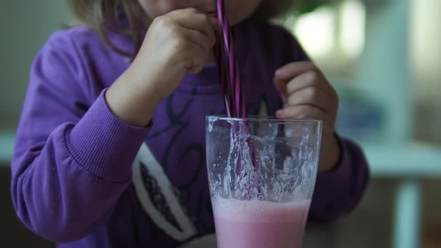 Fun little girl drinking red raspberry smoothie or cocktail from glass
