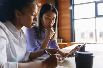 Two students sitting in co-working space, reading from digital tablet