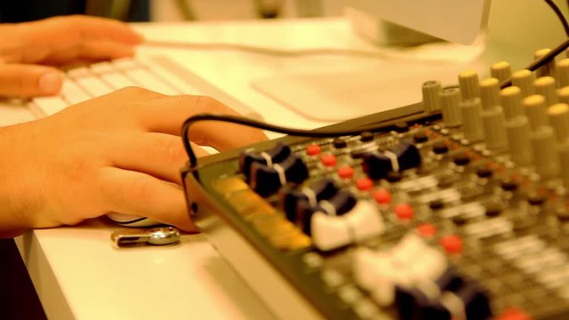 Focus chance from audio mixing console to hands of man using computer keyboard. Television production, film studio, sound recording set concepts. Professional engineer working with technology