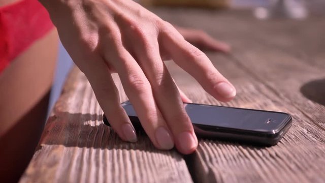 Close shot of woman's hand taking cell phone, smartphone lying on table, sexy woman's hips in lingerie on background