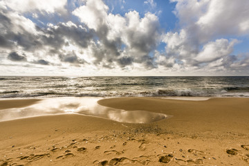 Sand beach with footprints against ocean and cloudy blue sky, Sardinia, Italy