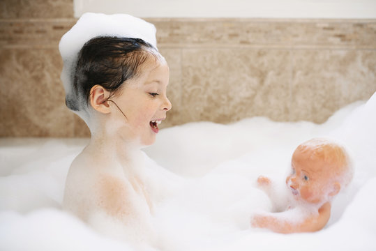 Girl sitting in a bubble bath playing with her doll
