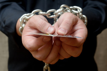 Hands of a man bound by a chain and holding a credit card. Credit bondage.