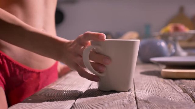Close shot of young sexy woman's hand taking cup and going away, standing in modern kitchen