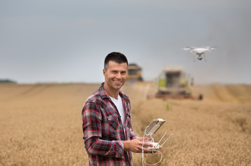 Farmer with drone in front of combine harvester - obrazy, fototapety, plakaty