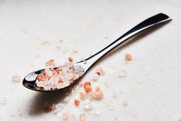 Black spoon of pink himalayan salt on marble table. Close up.
