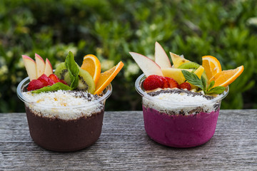 Two takeaway pots of acai with fresh fruit and mint leaves
