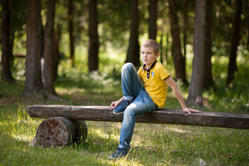 Fototapeta premium The boy is sitting on a bench in the forest.