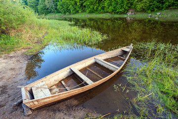 Obraz premium old wooden boat shore of river surrounded by forest at sunny summer day