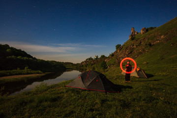 long exposure of tourist written with burning stick near tents at riverbank at summer night