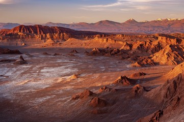 A white van crosses through a highway in a massive moon crater at Valle de la Luna, or the Moon Valley, Atacama desert, northern Chile, during sunset where rocky mountain appears golden. - Powered by Adobe