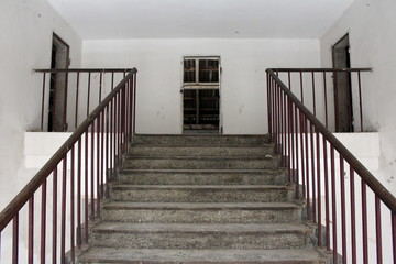 Concrete stariway with metal handrails leading to attic of dilapidated abandoned building with missing doors
