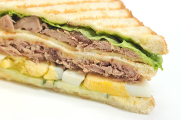 Sandwich of white bread triangular shape on white background. The filling of the sandwich consists of pieces of tuna, hard boiled eggs, lettuce leaves, cheese and sauce. Close-up. Macro photography.