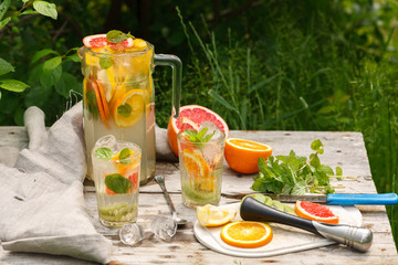 citrus lemonade in glass jug with mint. Orange. Grapefruit and lemon. On greenery background.