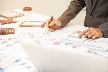 Businessman pen pointing graph chart and using a tablet for analyzing investment in his office.