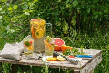 citrus lemonade in glass jug with mint. Orange. Grapefruit and lemon. On greenery background.