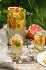 citrus lemonade in glass jug with mint. Orange. Grapefruit and lemon. On greenery background.