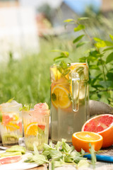 citrus lemonade in glass jug with mint. Orange. Grapefruit and lemon. On greenery background.