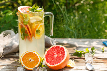 citrus lemonade in glass jug with mint. Orange. Grapefruit and lemon. On greenery background.