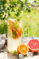 citrus lemonade in glass jug with mint. Orange. Grapefruit and lemon. On greenery background.