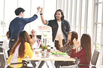  Young businessmen hi-fiving with congratulating calleagues in meeting at office