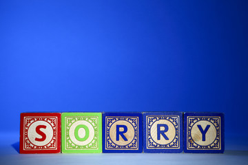 Wooden letter blocks on a blue background spelling out the word sorry