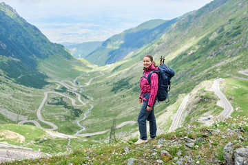 Girl with a backpack stands on a background of a picturesque landscape most beautiful road in Europe. Transfagarashan Highway, Romania, Ridge Fagaras