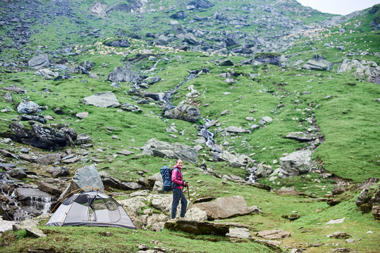 Shot of a woman hiker with a backpack and trekking poles standing near her tent in the mountains valley looking around copyspace relaxing resting hiking camping backpacking travelling exploring.