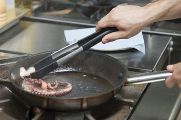 Cook cooks an octopus in a frying pan on a gas stove