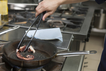 Cook cooks an octopus in a frying pan on a gas stove