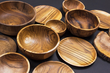 Wooden utensils for the kitchen, bowls, plates on a black background. The concept of natural dishes, a healthy lifestyle. Texture of wood. Wooden eco-ware