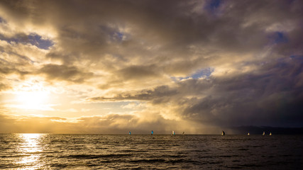 Obraz premium Colorful sailboats on a background of stormy clouds at sunset.