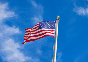 Waving flag of the United States against the blue sky with white  clouds.