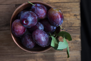 full rural bowl of large ripe blue plums on a wooden table