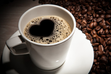 white cup of coffee with a picture of a heart on a background of roasted coffee beans