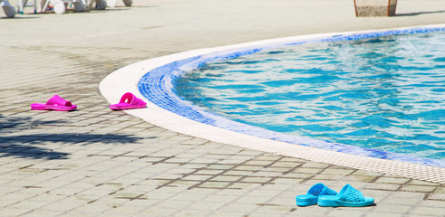 Summer background with blue and violet colored flip flops near the swimming pool. Colored flipflops...