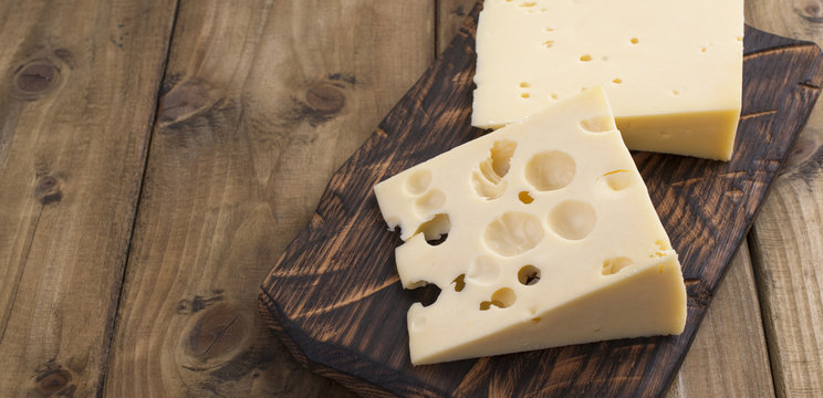 Traditional Dutch cheese with holes, on a vintage wooden board, wooden background. Dairy. Copy space. Above. Banner.